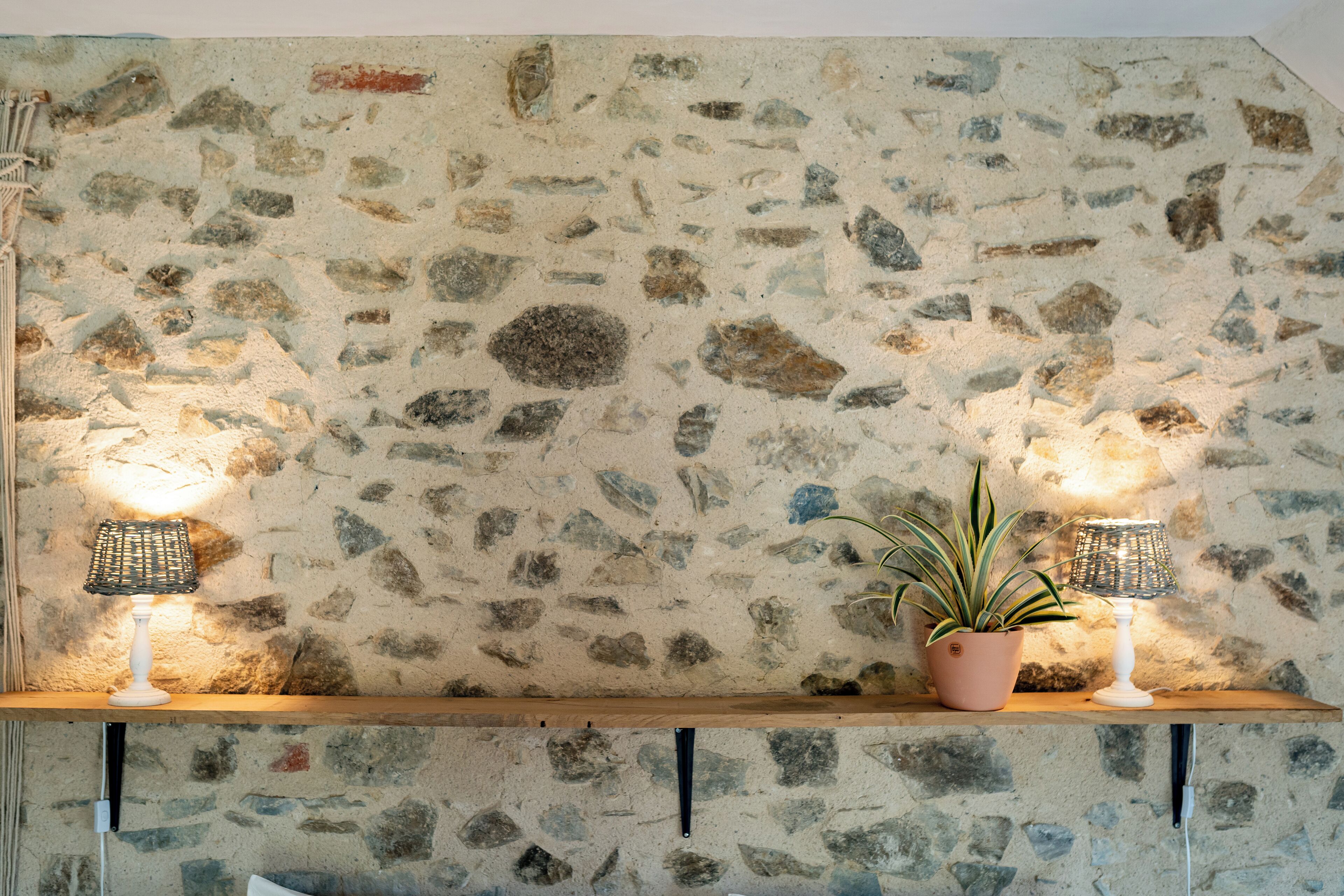 A stone wall with a shelf holding a potted plant and two wall-mounted lamps.
