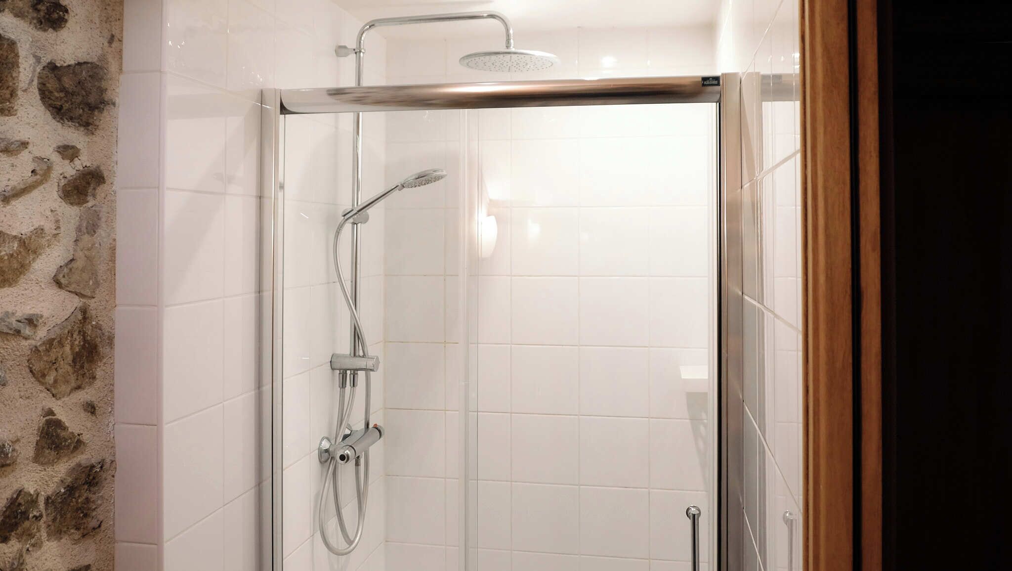 A glass-enclosed shower with a handheld showerhead and a wall-mounted faucet.