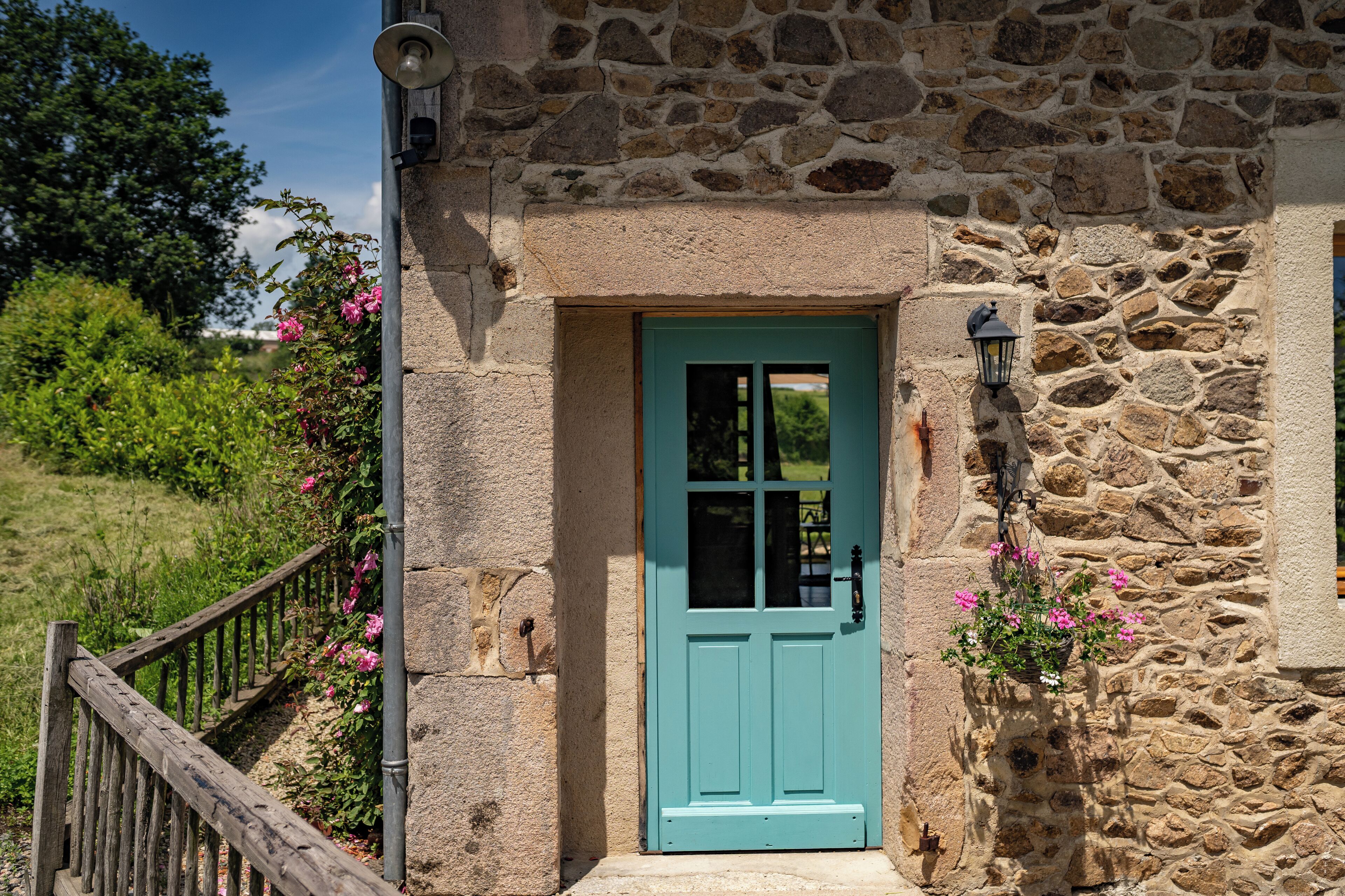A stone building with a turquoise door, a wooden fence, and a stone wall.
