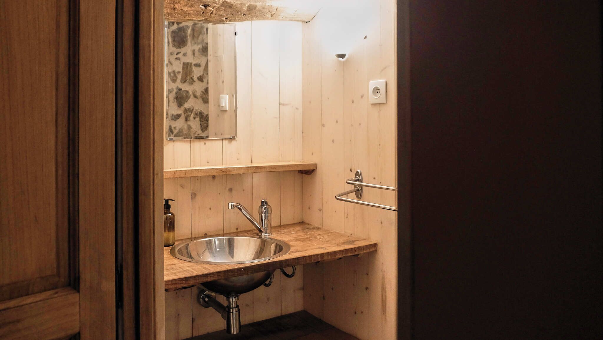 A small, wooden bathroom with a single sink, a mirror, and a towel rack.