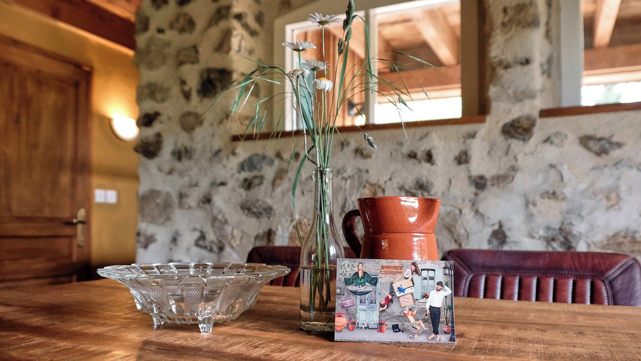 A wooden dining table with a glass bowl, a clear vase with green plants, and a ceramic jug.