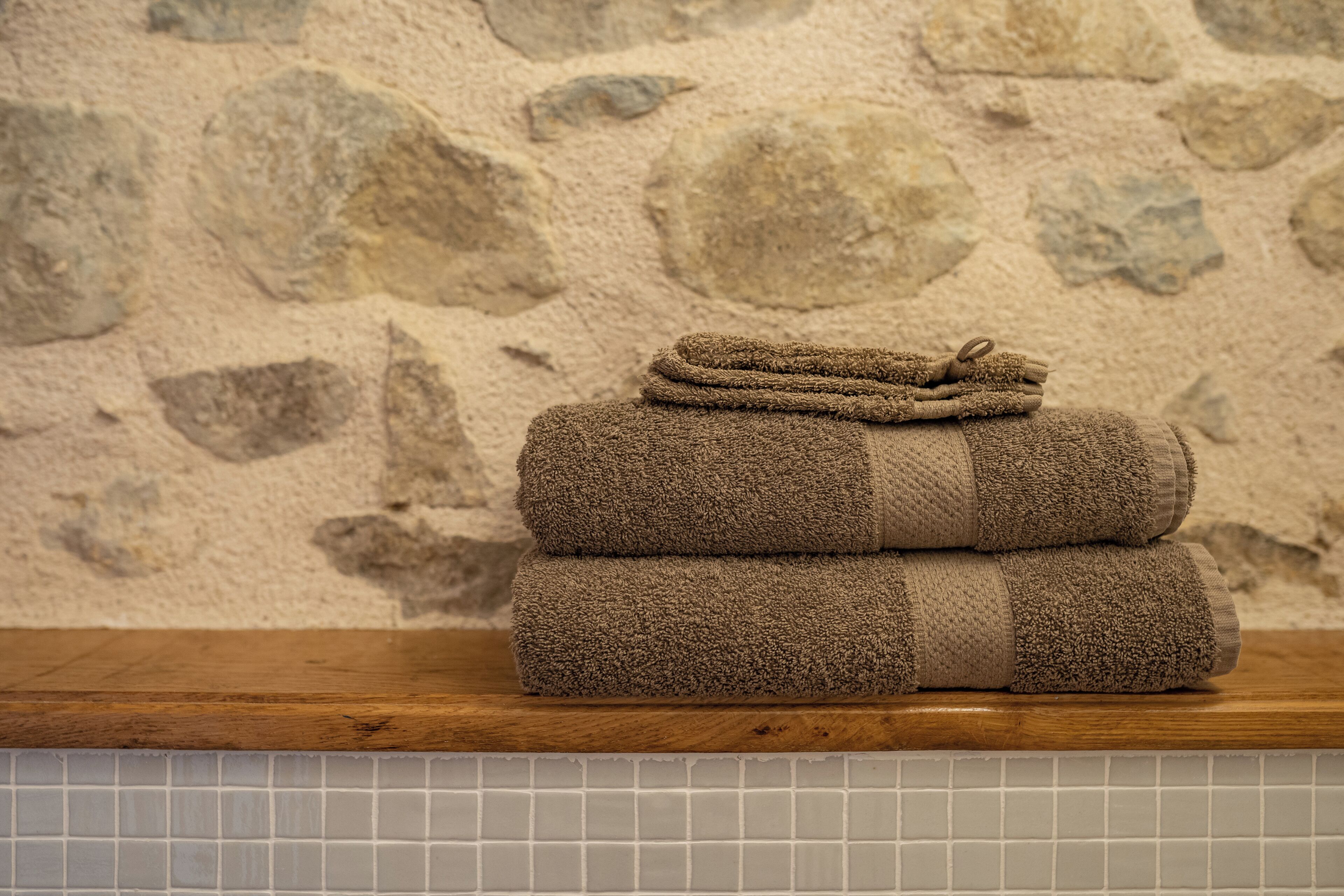 A stack of folded towels on a wooden shelf against a stone wall.