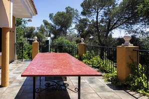 Une table rouge avec un cadre en métal, placée sur une terrasse carrelée, agrémentée d’une rambarde noire et de piliers jaunes.