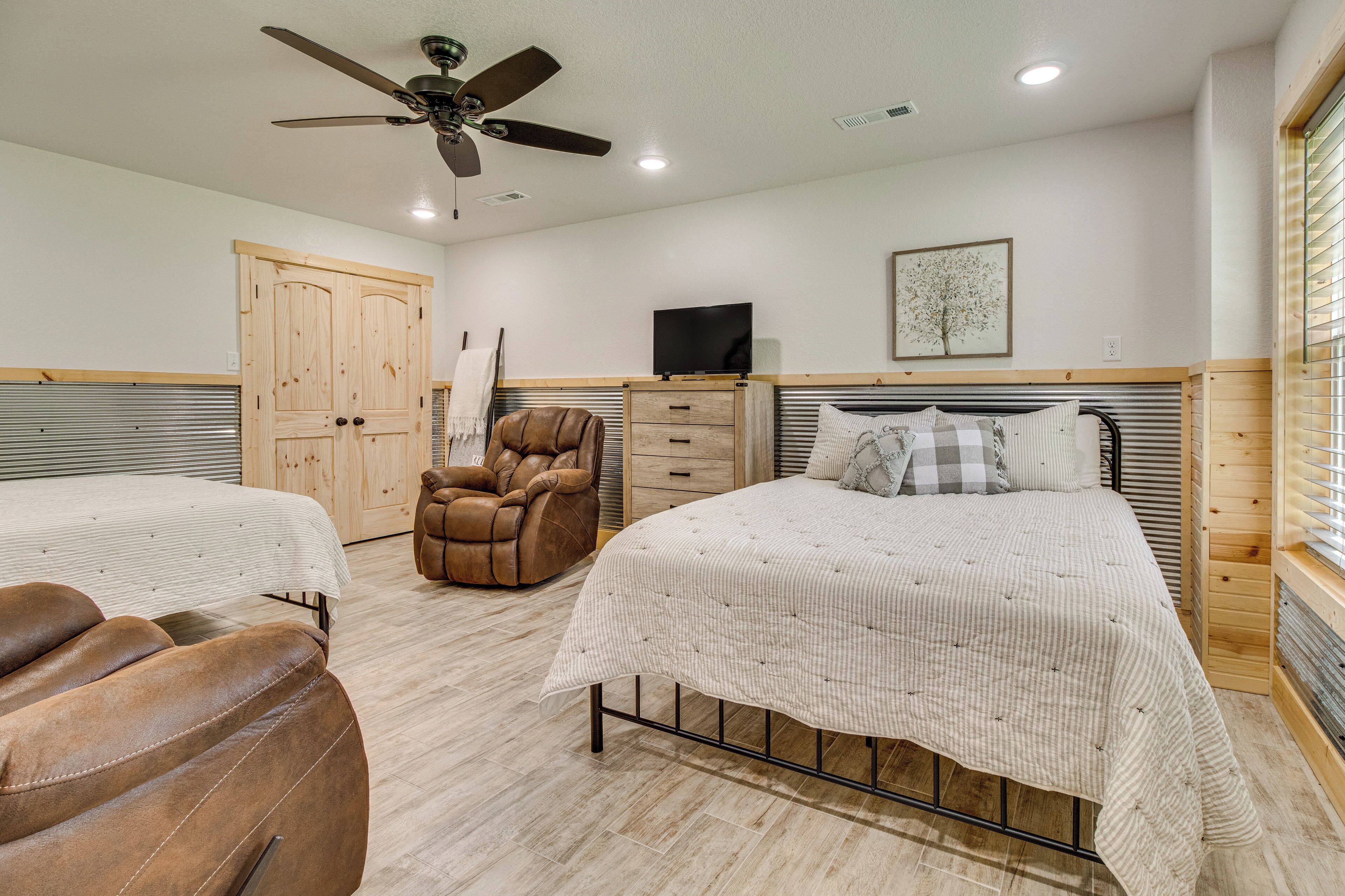 A bedroom with two beds, a ceiling fan, a television, and a wooden wardrobe.