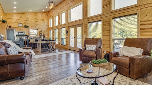 A spacious living area with a wooden interior, leather sofas, a glass coffee table, and a kitchen in the background. - Waterfront Cabin on White River w/ Deck + Patio! (Mountain Home)