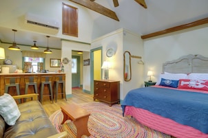 Una habitación acogedora con cama, sofá, comedor con sillas y una cocina al fondo.