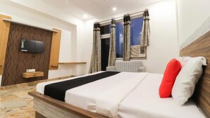 Una habitación de hotel moderna con una cama grande, un televisor de pantalla plana montado sobre un panel de madera, una ventana con cortinas y un piso de mármol.