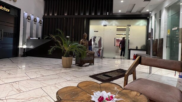 Un vestíbulo con piso de mármol, una mesa de madera con un arreglo floral, una estatua de Buda y una lámpara moderna.