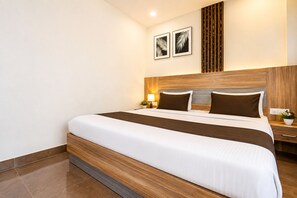 A hotel room with a large bed, wooden headboard, two bedside tables with lamps, and framed artwork on the wall.