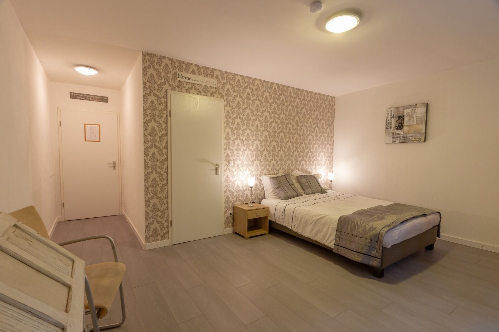 Un dormitorio con cama, mesitas de noche, una silla y una puerta.