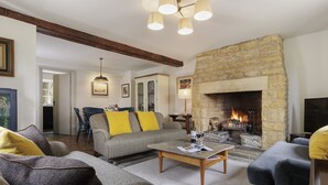 A cozy living room with a stone fireplace, a dining area with blue chairs, and a sofa with yellow cushions. - Charming dog friendly cottage - Bank Cottage (Longborough)