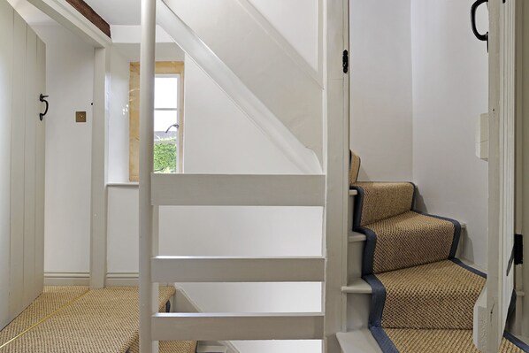 A staircase with white railings and a patterned chair in a room with white walls and a window.