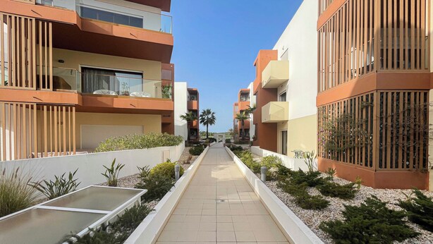Un edificio residencial moderno con un paseo central, balcones y un jardín.
