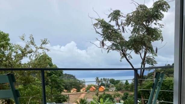 Un balcón con dos sillas verdes y una pequeña mesa, con vistas a una zona residencial con casas y vegetación.