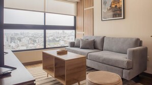A modern living room with a grey sofa, a wooden coffee table, and a view of a cityscape through large windows. - w Elegant 1BR Retreat in the Heart of San Isidro (Lima)