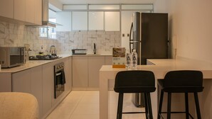 A modern kitchen with a built-in microwave, stove, oven, and stainless steel refrigerator. There are two black bar stools and a white island with a sink. - Magnificent 3BR in the Heart of Barranco (Lima)