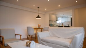 A modern living room with a white sofa, two armchairs, a small table, and a pendant light. A kitchen is visible in the background. - Magnificent 3BR in the Heart of Barranco (Lima)