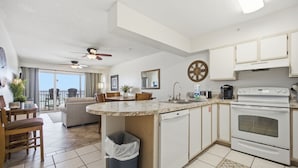 A modern kitchen with a central island, a built-in oven, and a dining area with a sofa and chairs. - Emerald Towers West #4002 - Beachfront - 2 King Suites - Free Beach Service! (Fort Walton Beach)