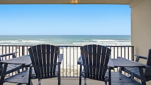 A balcony with two chairs and a table, overlooking a beach with the ocean and a clear sky. - Emerald Towers West #4002 - Beachfront - 2 King Suites - Free Beach Service! (Fort Walton Beach)