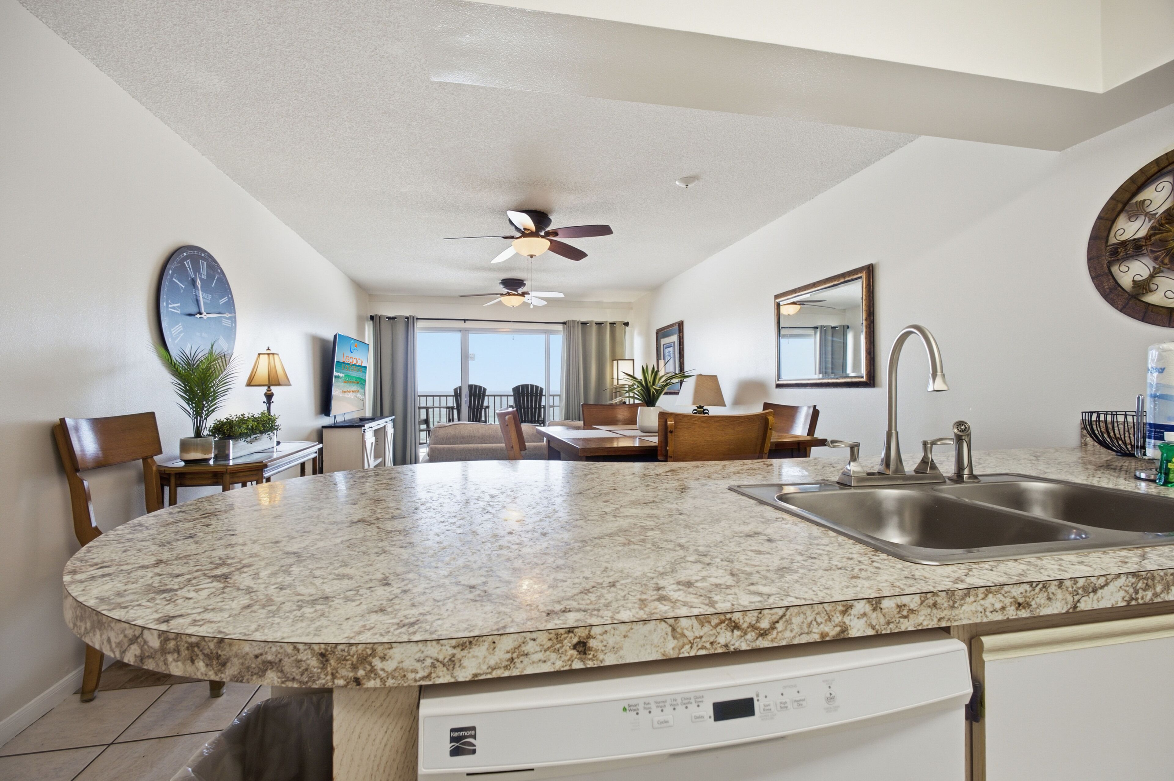 A kitchen with a built-in dishwasher, a dining area with chairs, a ceiling fan, and a large window.