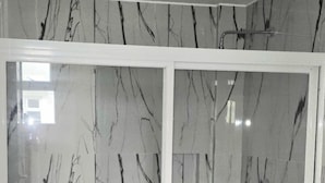 A bathroom with a marble wall, a white toilet, and a shower area with a glass door. - Leribi Hotel and Restaurant (Tagaytay)