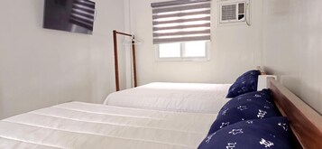 Una habitación con una cama, un perchero, una ventana con persianas y un equipo de aire acondicionado.