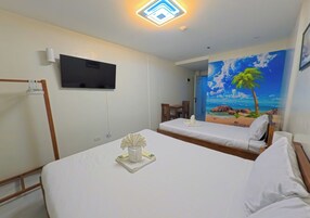 Habitación de hotel con dos camas, un televisor de pantalla plana montado en la pared y un mural de playa en la pared contigua.