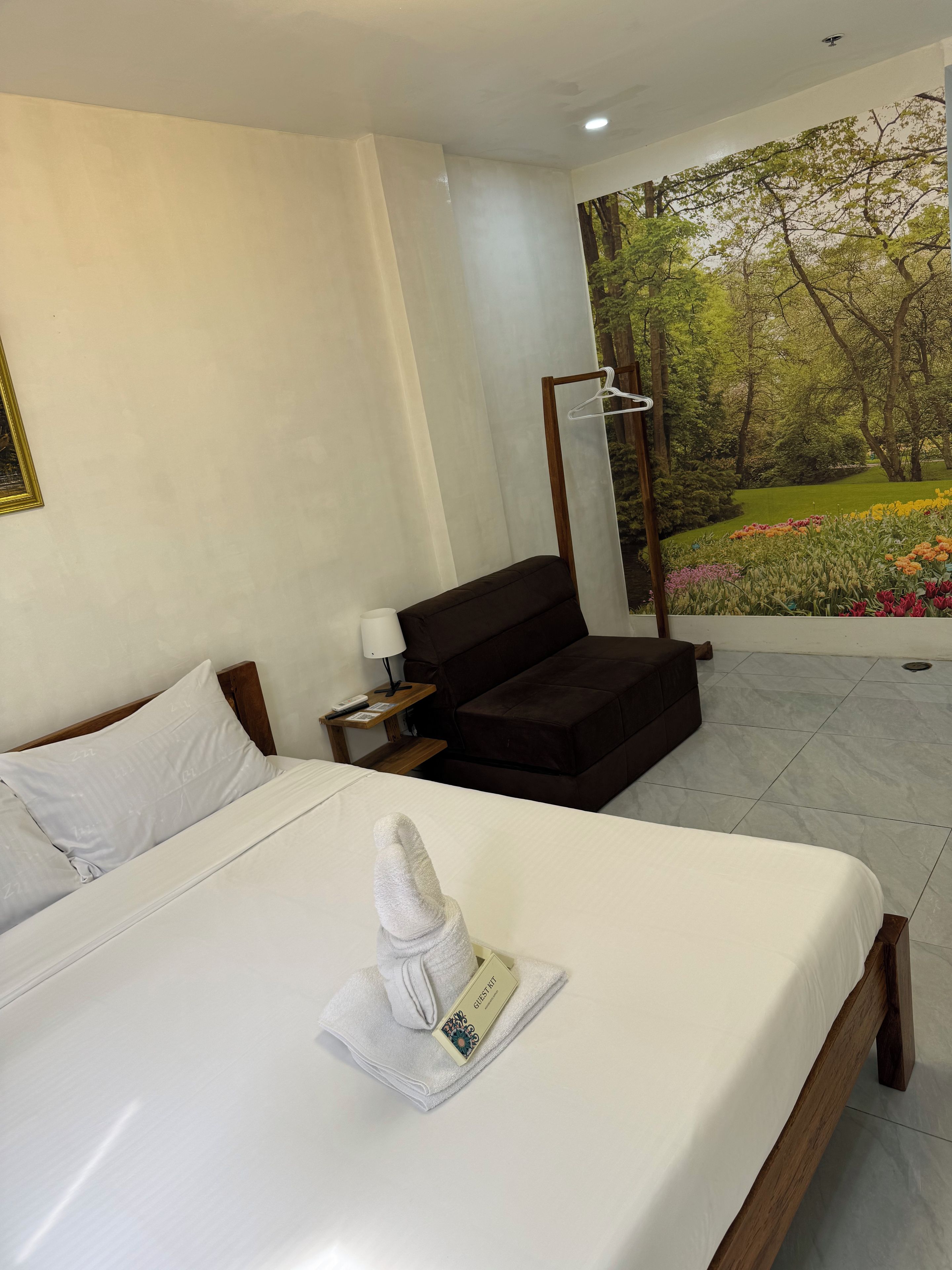 Una habitación de hotel con una cama, un sofá, un cuadro de un jardín y una toalla con una etiqueta.