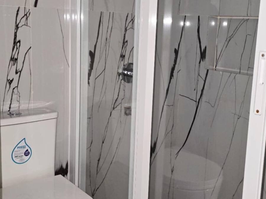 Et badeværelse med toilet, glasvæg omkring brusebad og væg med marmorlook.