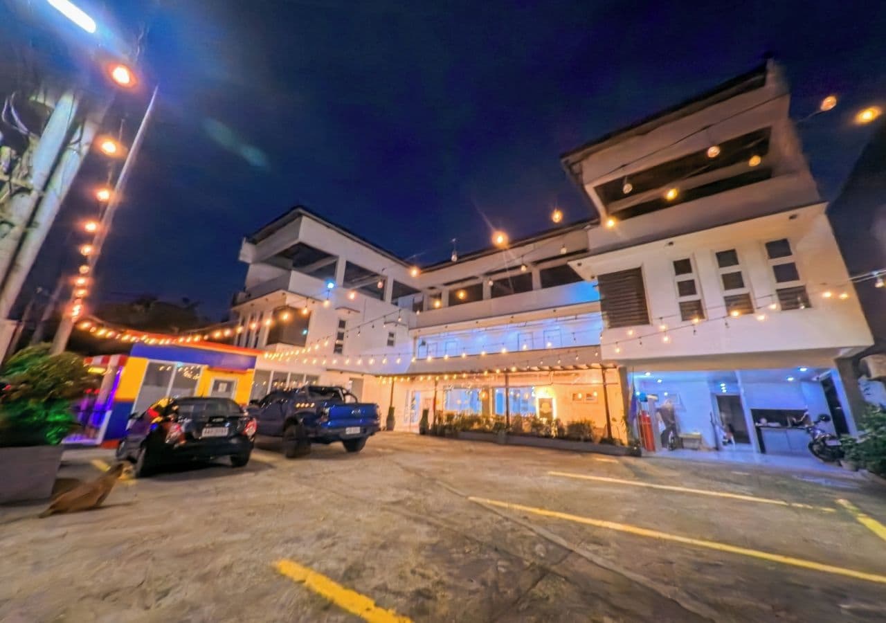 Un hotel con área de estacionamiento, varios vehículos y una entrada bien iluminada.