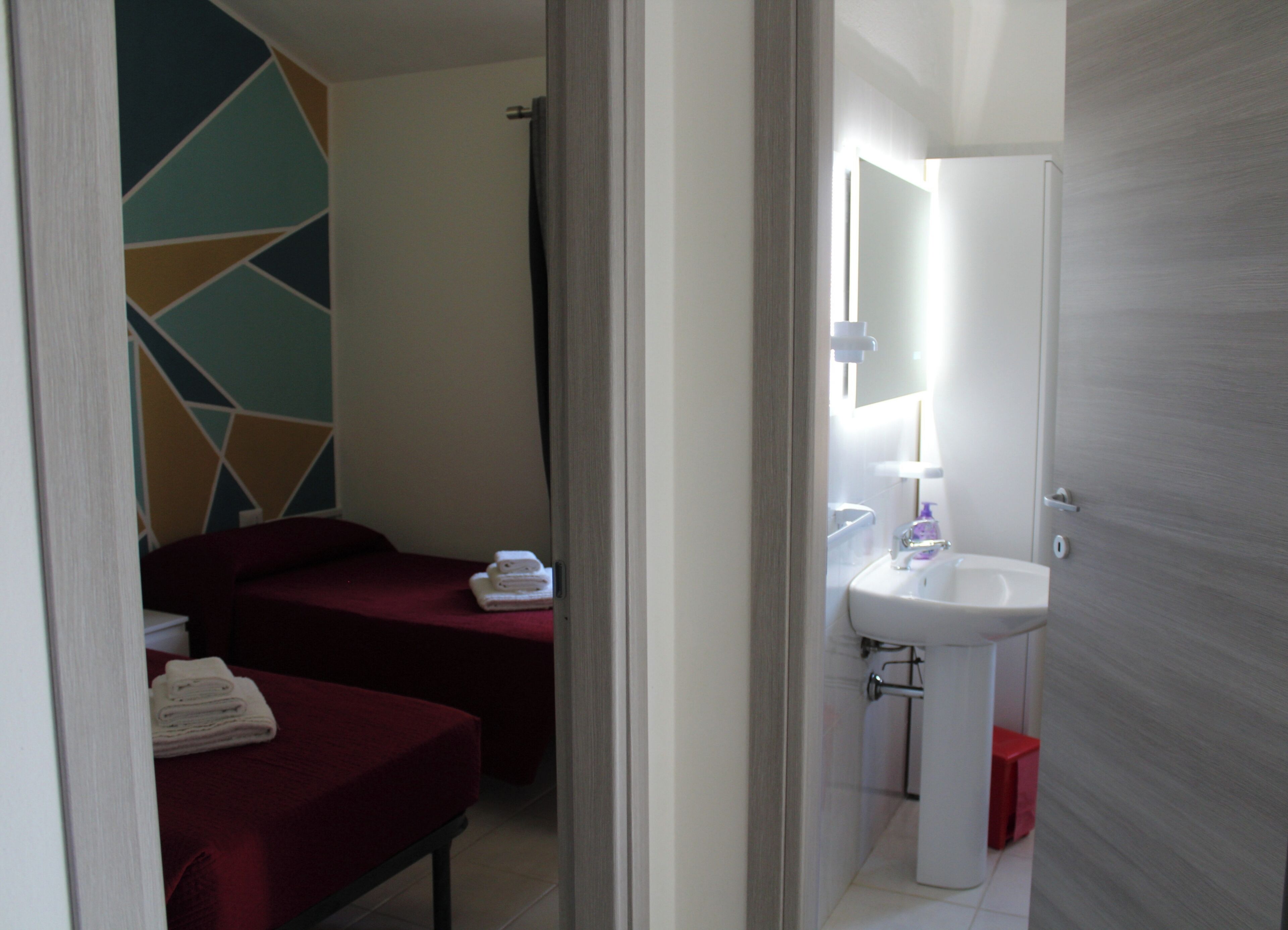 A bathroom with a sink, mirror, and two beds with red bedding.