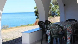 A covered outdoor seating area with a view of the sea, featuring a table and chairs.