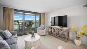 En moderne stue med sofa, lænestol, fjernsyn og en balkon med havemøbler.