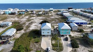 A coastal residential area with houses on stilts, a beach in the background, and a clear sky.