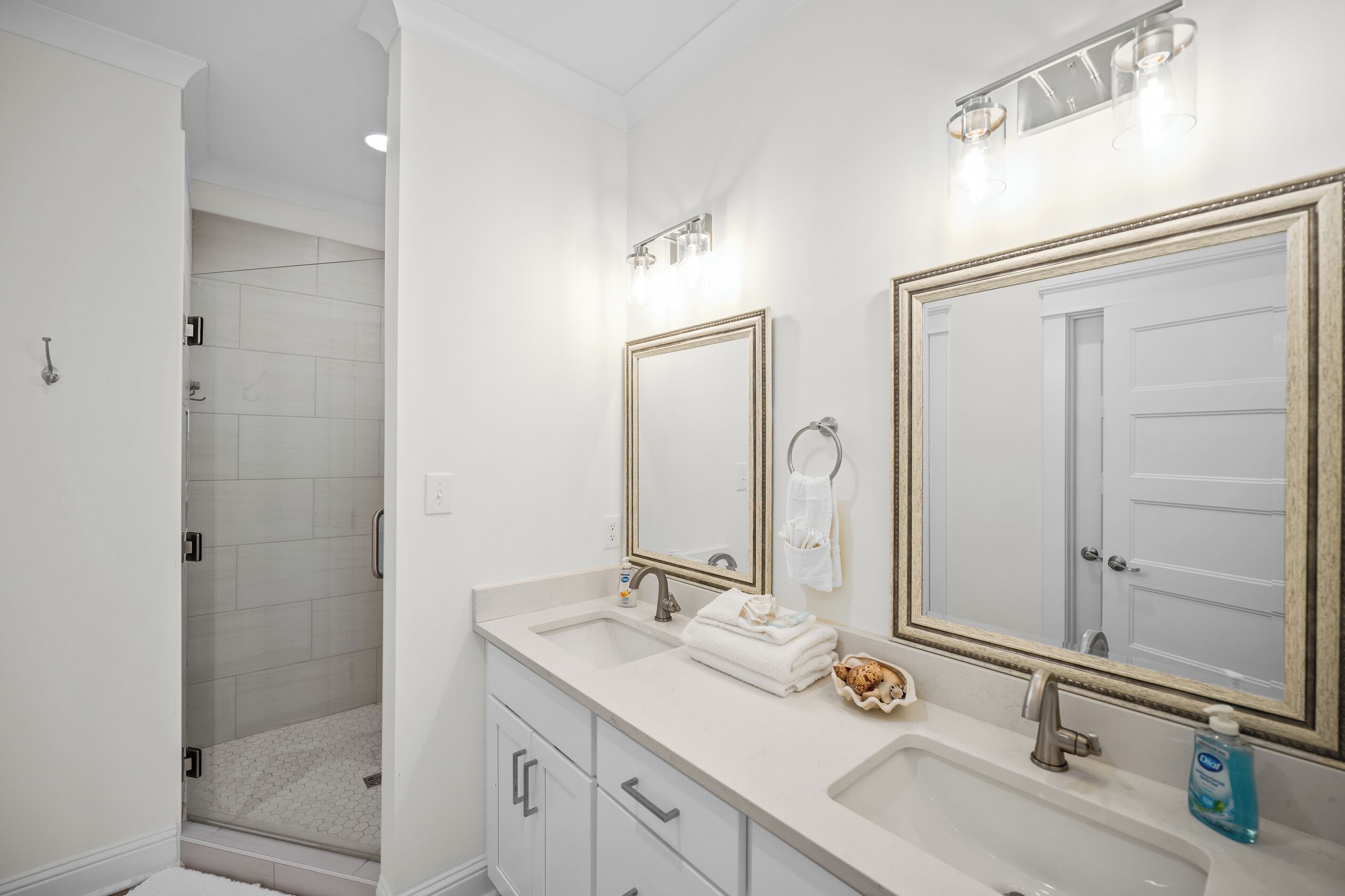 Une salle de bain avec deux lavabos, une douche et deux grands miroirs dotés de cadres dorés.