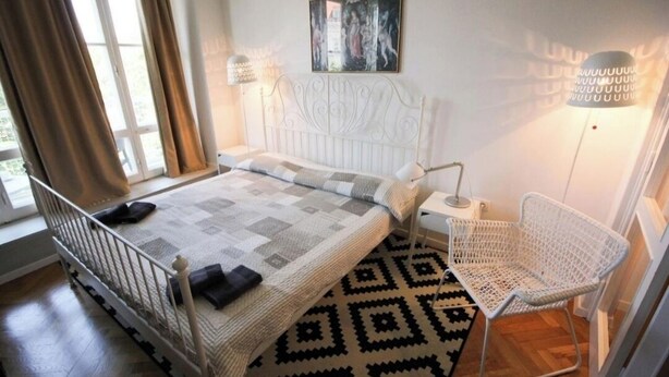 Une chambre avec un lit blanc, un tapis à motifs, une chaise blanche et un tableau accroché au mur.