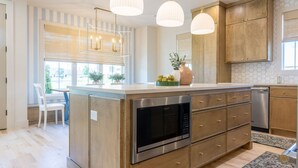 Une cuisine moderne avec des meubles en bois, un four en acier inoxydable et des luminaires suspendus.