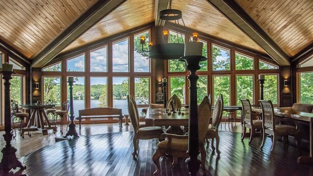A spacious dining area with high ceilings and large windows offering views of a lake and trees.