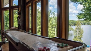 A shuffleboard table with pucks in red, green, and white, and a view of a lake through large windows.