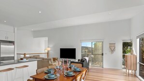 A modern kitchen with a large refrigerator, a dining area with a wooden table and chairs, a flat-screen TV, and a sliding glass door leading to a balcony. - Chloe Retreat in Cowes (Cowes)