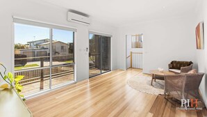 A spacious living area with a wooden floor, a sofa, a dining table, and large sliding glass doors leading to a balcony. - Chloe Retreat in Cowes (Cowes)