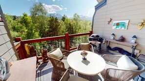 A balcony with wicker furniture, a grill, and a view of trees and mountains.