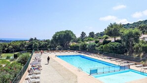 A rectangular swimming pool with a tiled deck, surrounded by lounge chairs and umbrellas. - Villa 3 façades garden terrace and sea view, swimming pool and club house, tennis court (La Croix-Valmer)