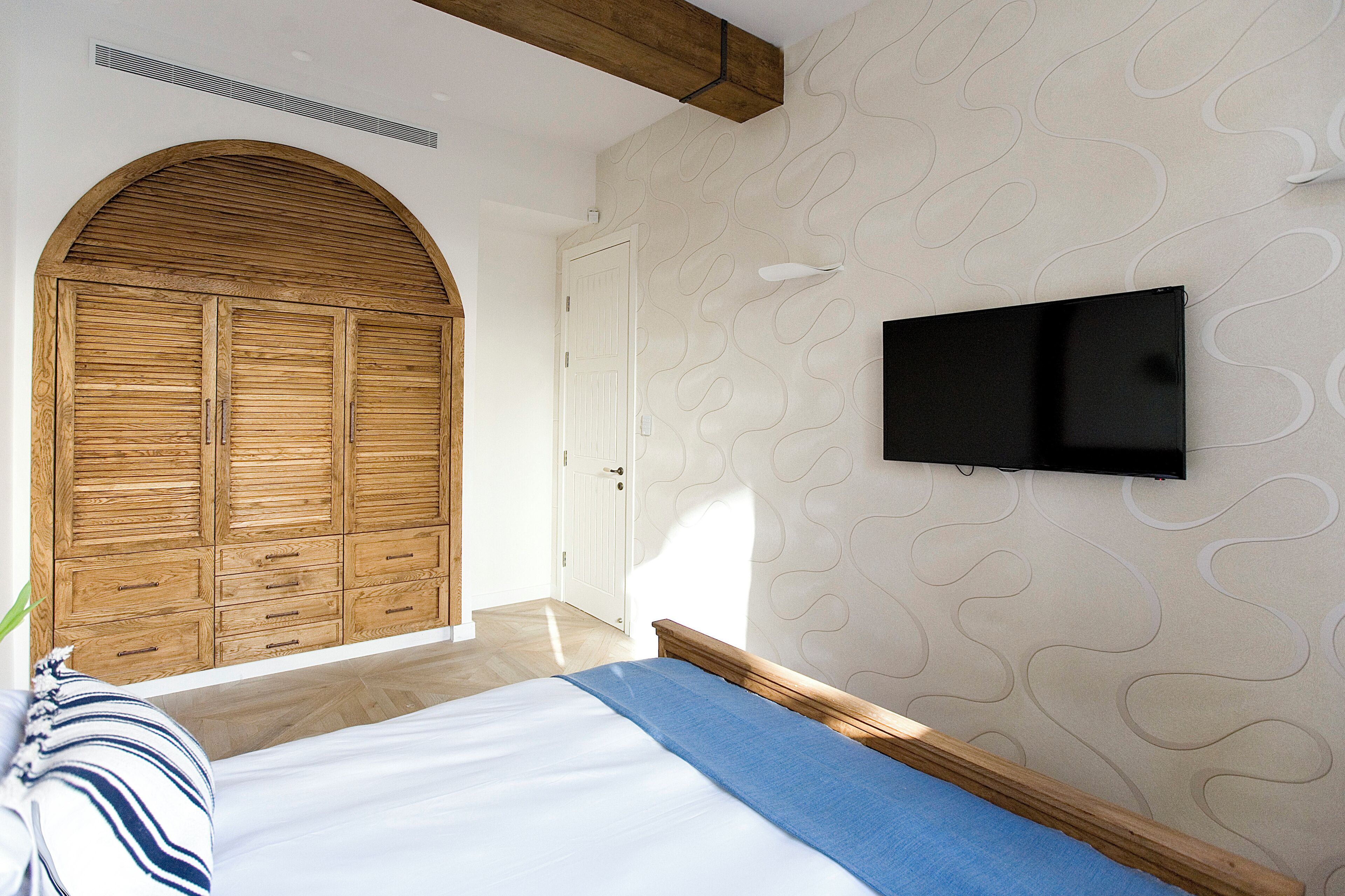 Un dormitorio con cama, armario de madera y televisor montado.