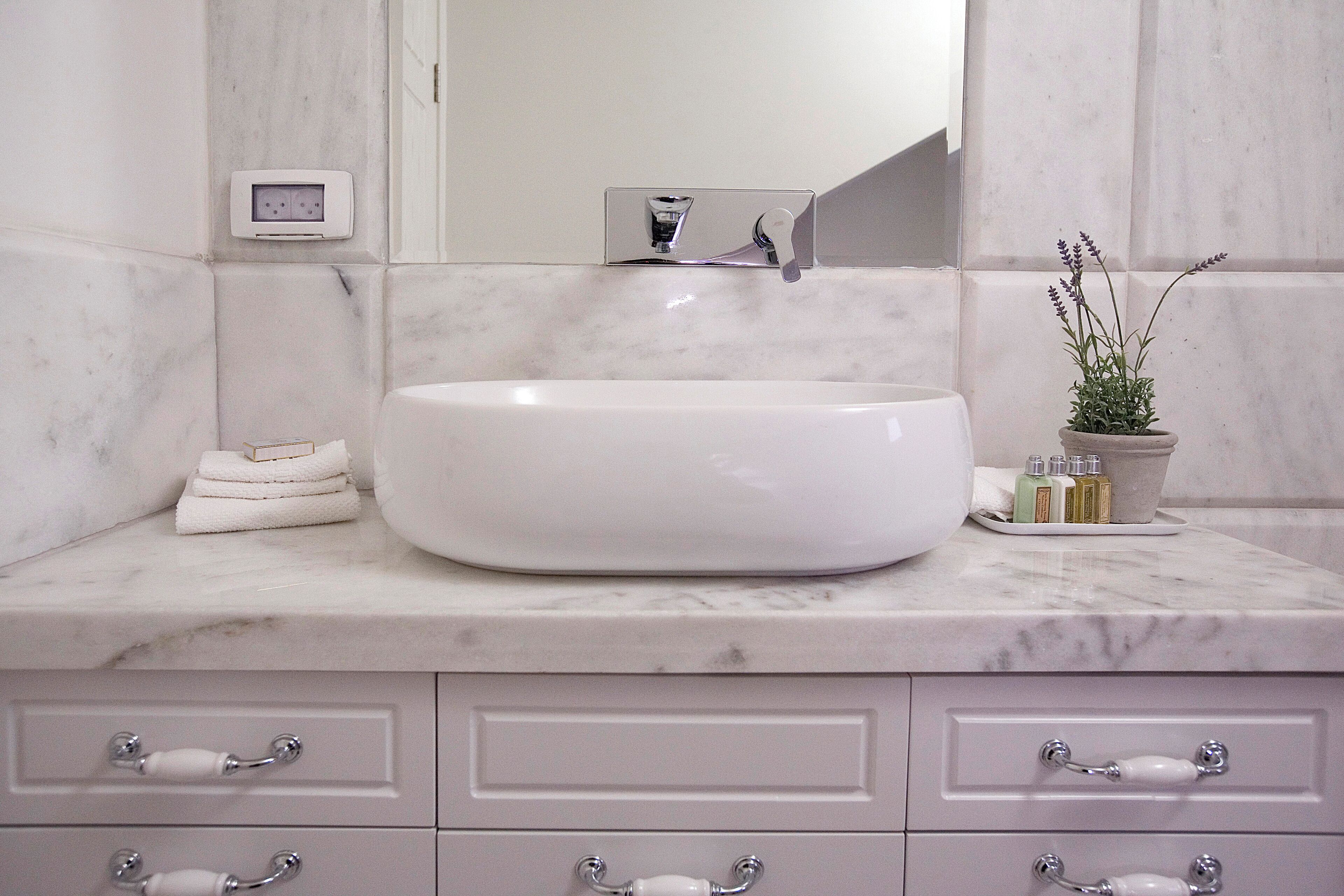Un baño con lavamanos blanco, encimera de mármol y una planta en maceta.