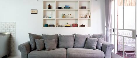 Un salon avec un canapé gris, une table basse en bois sur laquelle repose un livre, et une étagère blanche contenant divers objets.