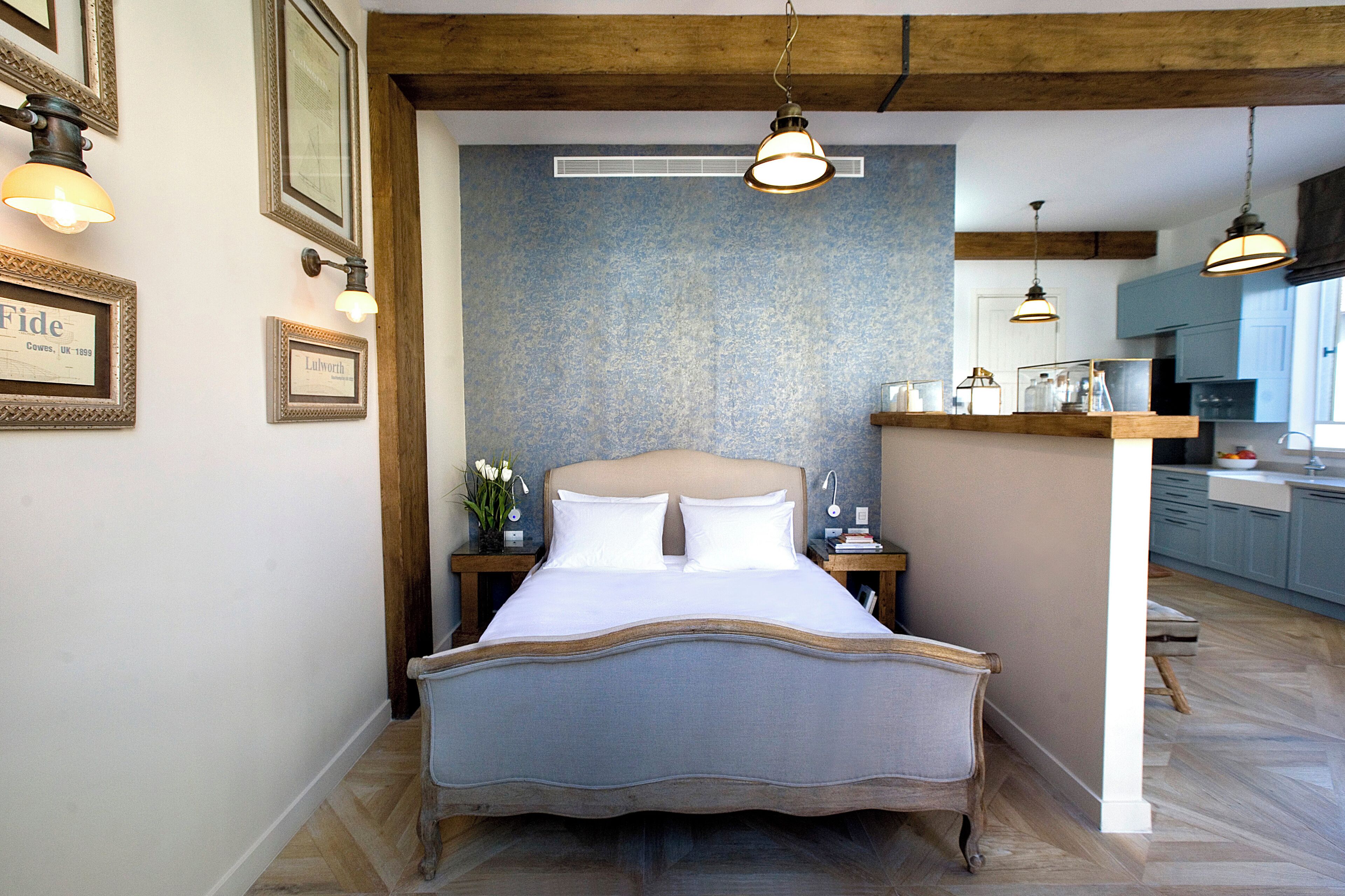 A bedroom with a bed, bedside tables, framed pictures, and a view of the kitchen.