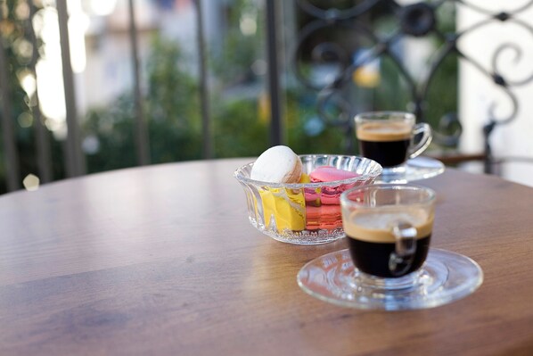 Una mesa de madera redonda con un bol de vidrio que contiene macarons y una taza de café.