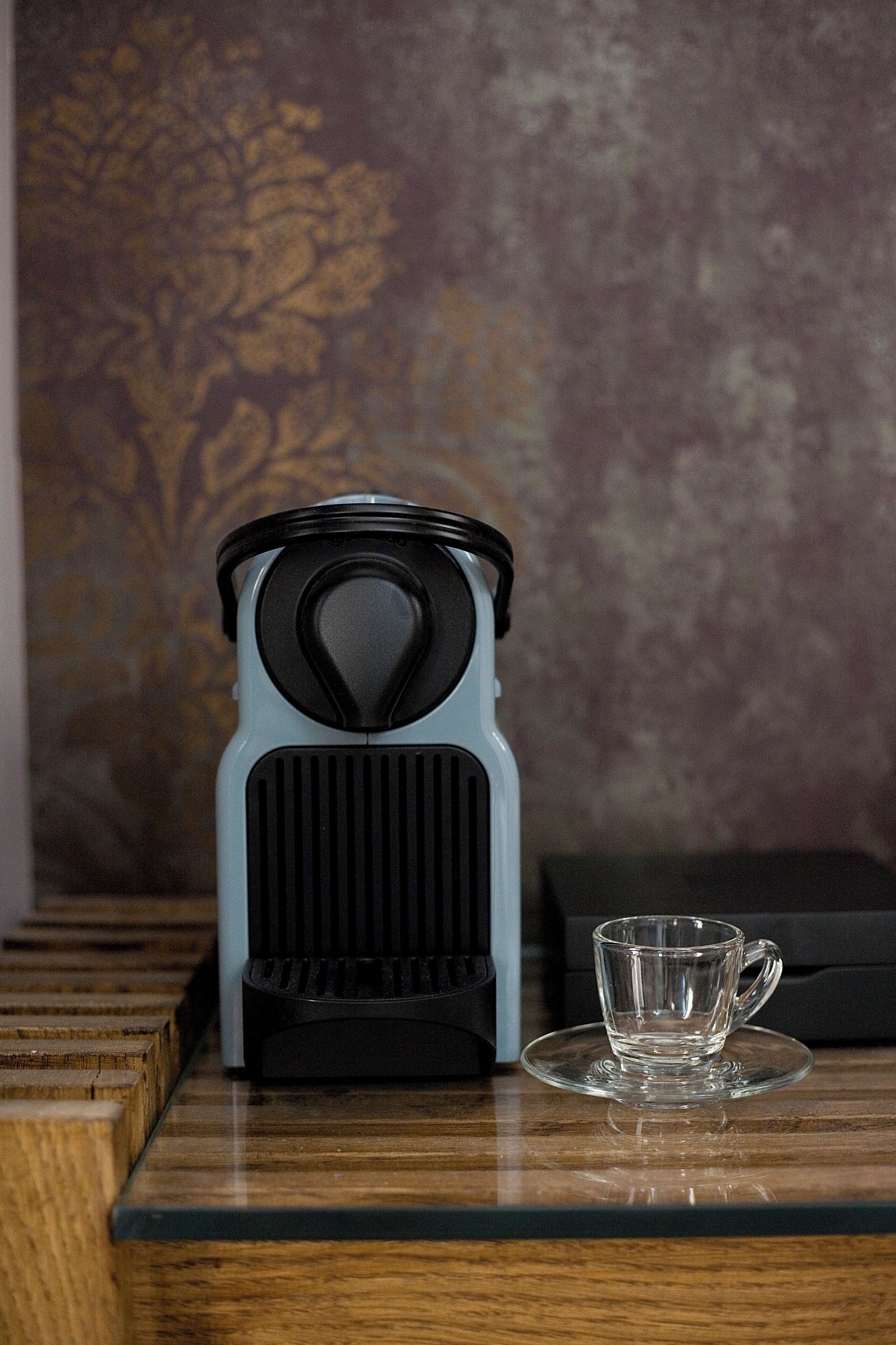 A coffee maker on a wooden surface with a glass cup beside it.