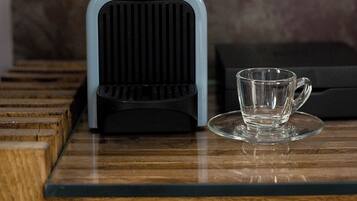 A coffee maker on a wooden surface with a glass cup beside it.